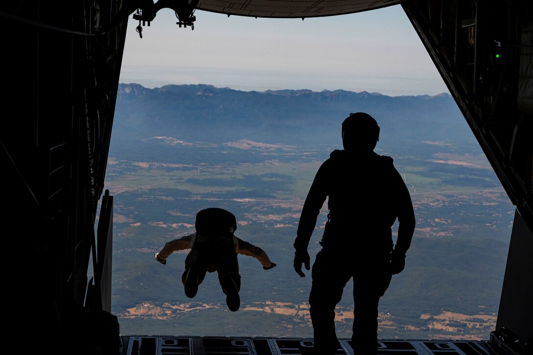 One service member jumps from a plane while another one watches.