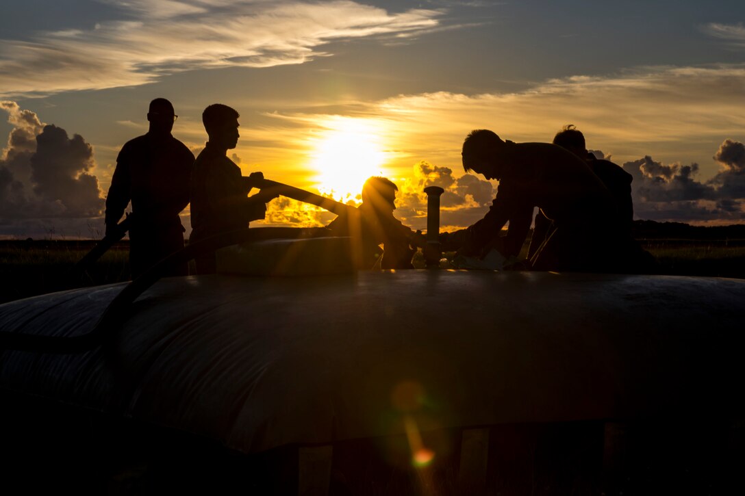 A silhouette of Marines working on a fuel line.