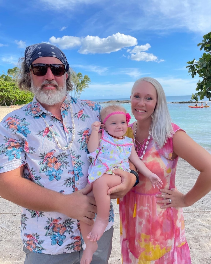 Husband, wife and daughter pose for a photo on the beach.