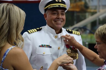 PENSACOLA, Fla. (Aug. 18, 2022) Family members of Capt. Daniel “Jinx” Testa place the command pin on Testa’s uniform after he assumed command of Naval Education and Training Security Assistance Field Activity (NETSAFA) during a change of command ceremony at the National Naval Aviation Museum, Aug. 18, 2022. Testa relieved Capt. David Stallworth as NETSAFA’s commanding officer. NETSAFA is the U.S. Navy’s agent for Navy education and training for international military students. (U.S. Navy photo by Wade Buffington)