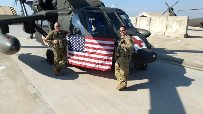 Chief Warrant Officer 4 Kayce Clark and another pilot stand in front of a helicopter with an American flag.