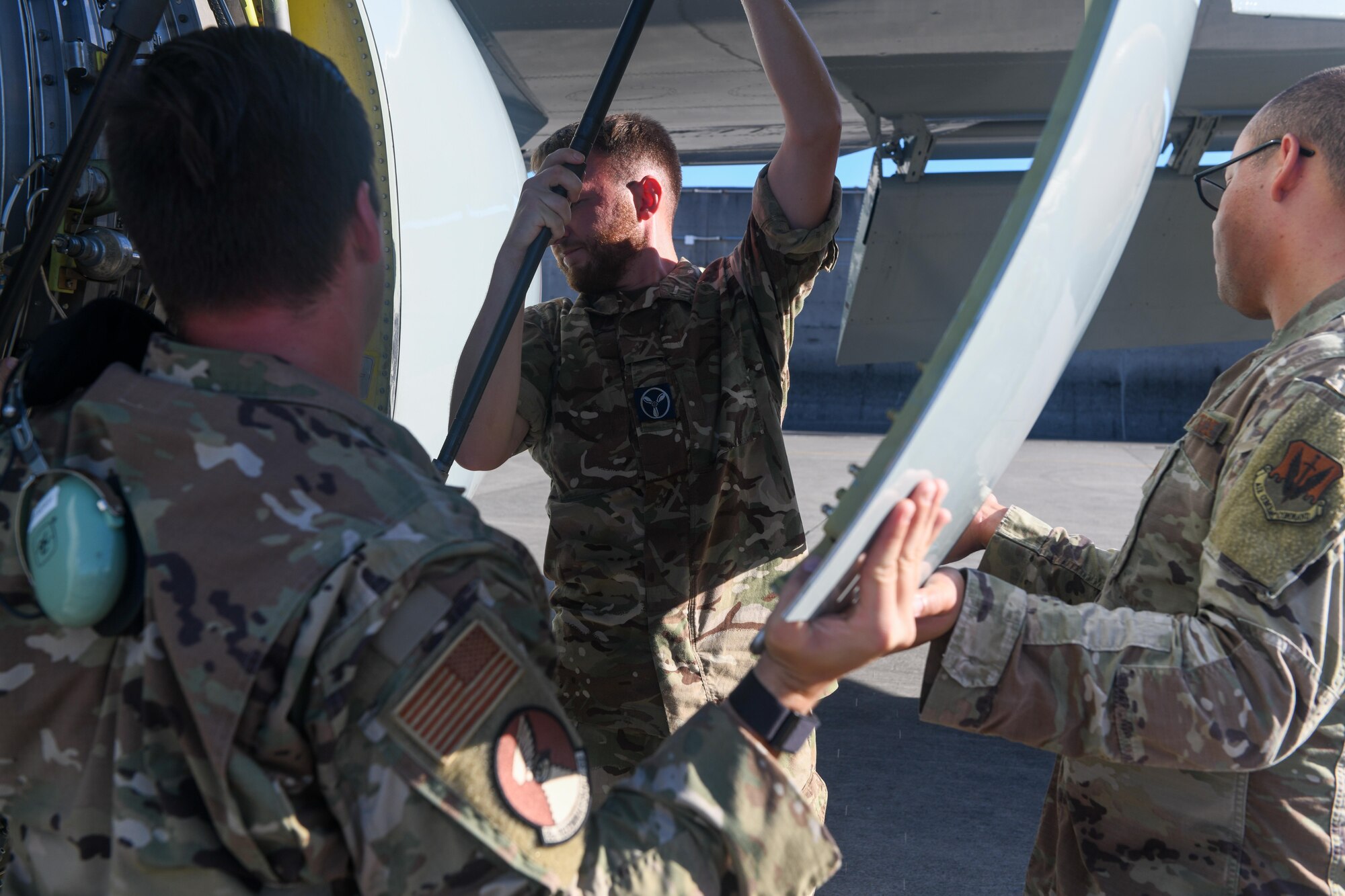 Airmen and an aviator replace a panel on an aircraft.