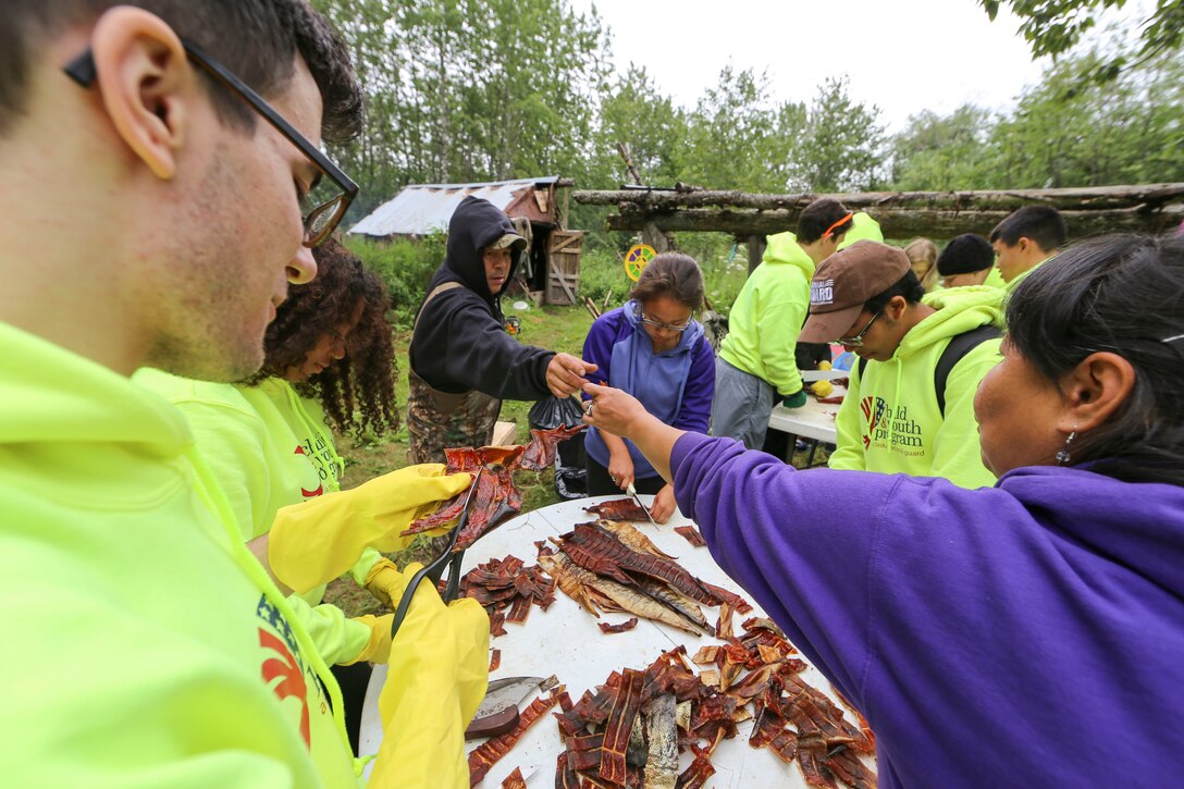 Rachel Sallaffie, right, hands a salmon strip to her husband, Sgt. 1st Class Joseph Sallaffie, then a staff sergeant, while demonstrating the process of drying and cutting salmon strips to participants of the Alaska National Guard Warrior and Family Services cultural camp at thier subsistence fish camp on the shores of the Kuskowim River near Bethel, July 21, 2016. The youth learned the importance of subsistence living during the five-day program that focused on cultural-based service and learning projects.