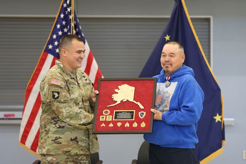Alaska Army Guard Maj. Walter Hotch-Hill, 49th Missile Defense Battalion (Ground-based Midcourse Defense), presents a gift to 1st Class Joseph Sallaffie, 1st Battalion, 297th Infantry Regiment, during a retirement ceremony at the National Guard armory in Bethel, Aug. 19, 2022.