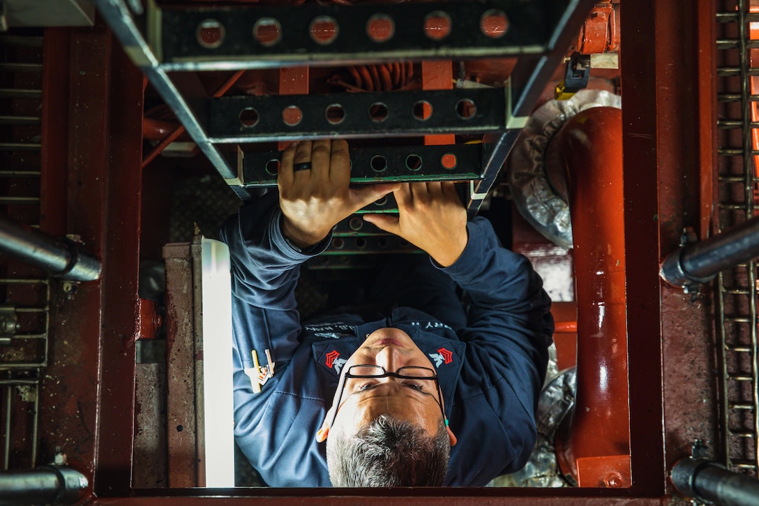 A sailor climbs a ladder in the engine room of a ship.