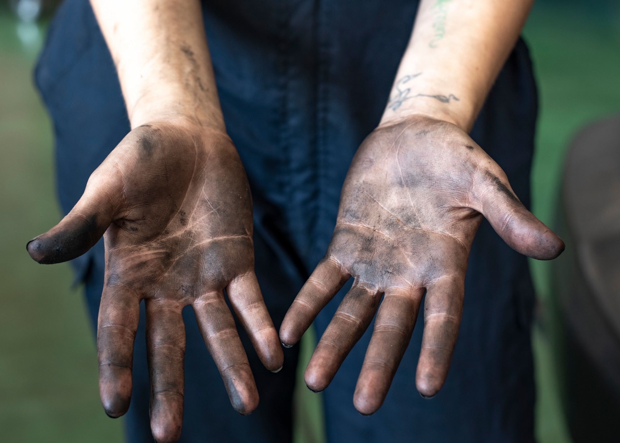 Airman 1st Class Maddison Stockman, 374th Logistics Readiness Squadron Vehicle Maintenance Flight apprentice, reveals her oil-covered hands after repairing a government vehicle at Yokota Air Base, Japan, Aug. 17, 2022.