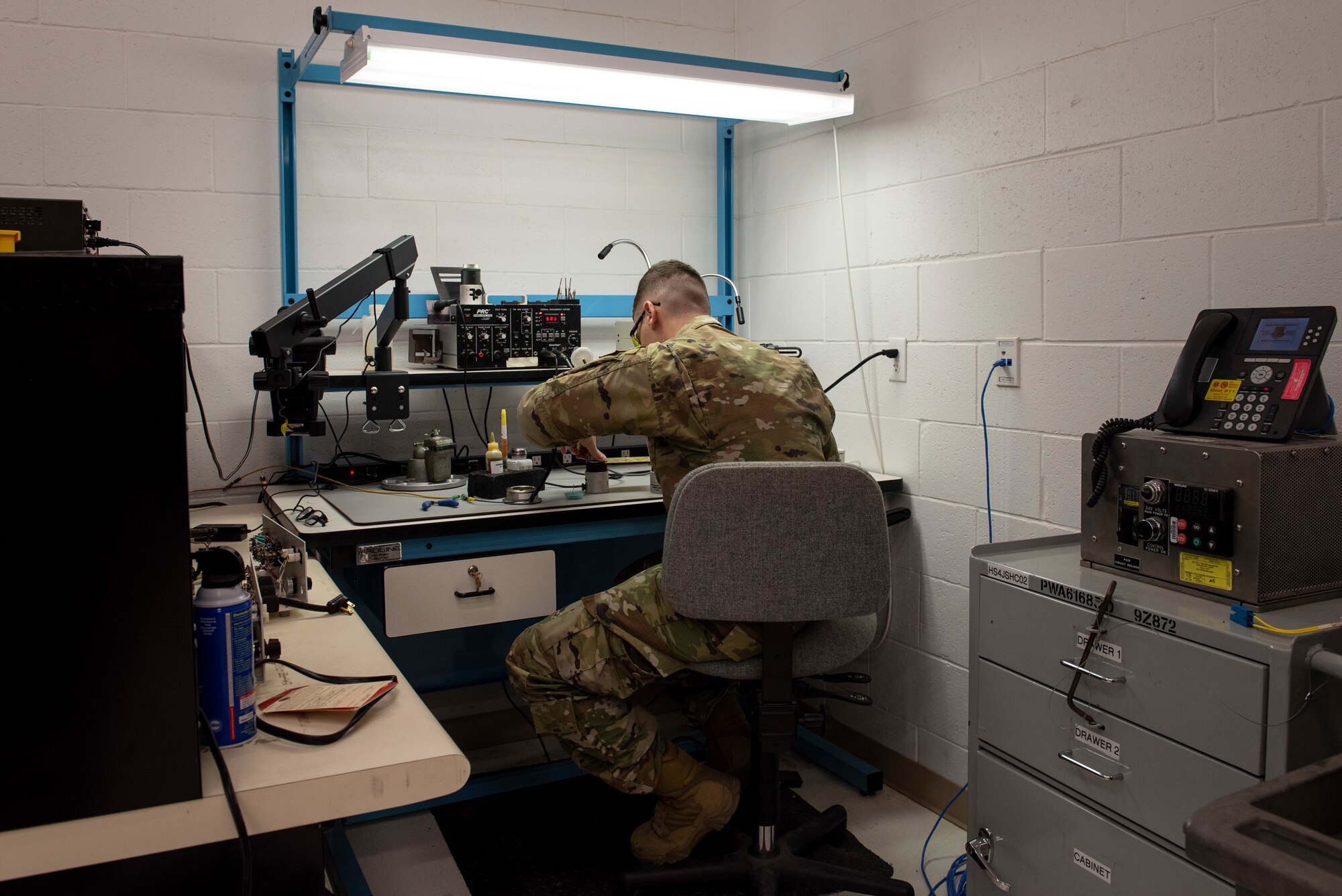 Staff Sergeant Brody Graham in green ocp's, sits on a grey chair in a work station.