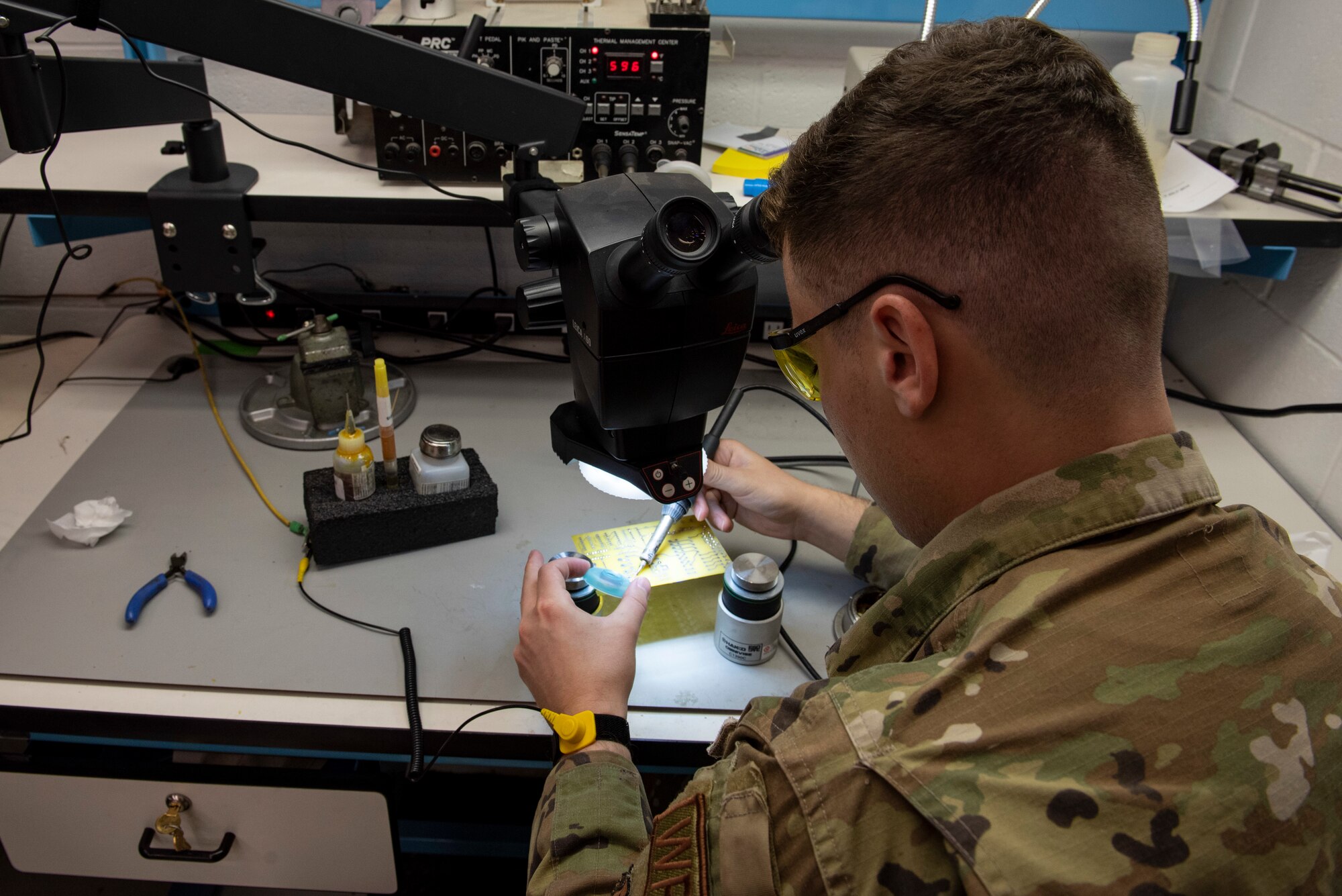 Staff Sergeant Brody Graham in green ocp's works on restoring a yellow computer processing unit.