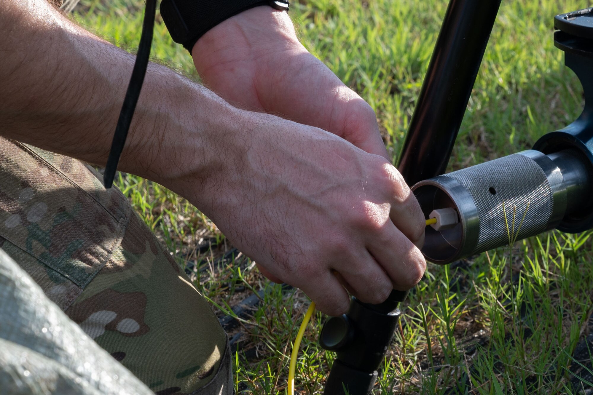 An Airman connects a yellow cord to a explosive tool.