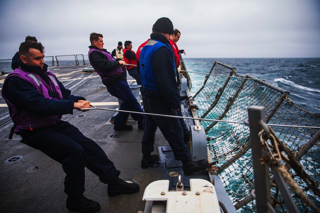 Several sailors pull up flight nets on a ship in the ocean.