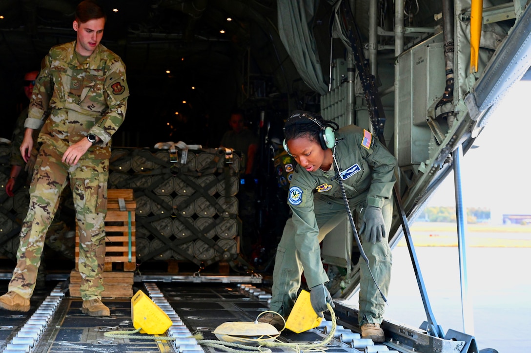 Two airmen stand inside the cargo bay of an aircraft.