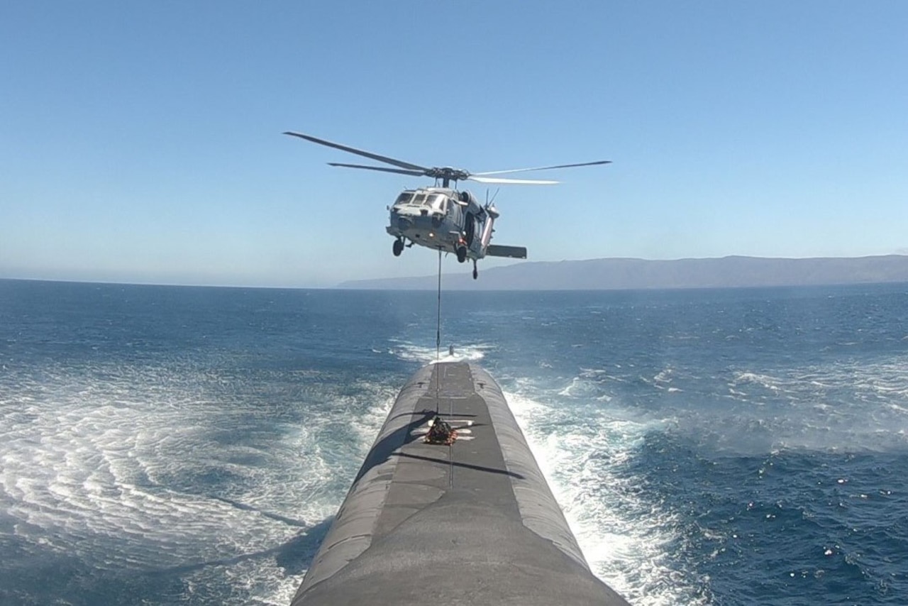 A helicopter hovers above a submarine at sea.