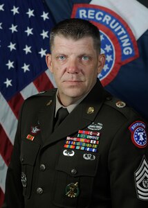 Man in U.S. Army uniform standing in front of two flags.