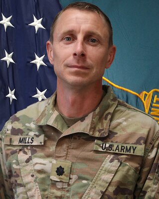 Soldier in  uniform standing in front of flags.