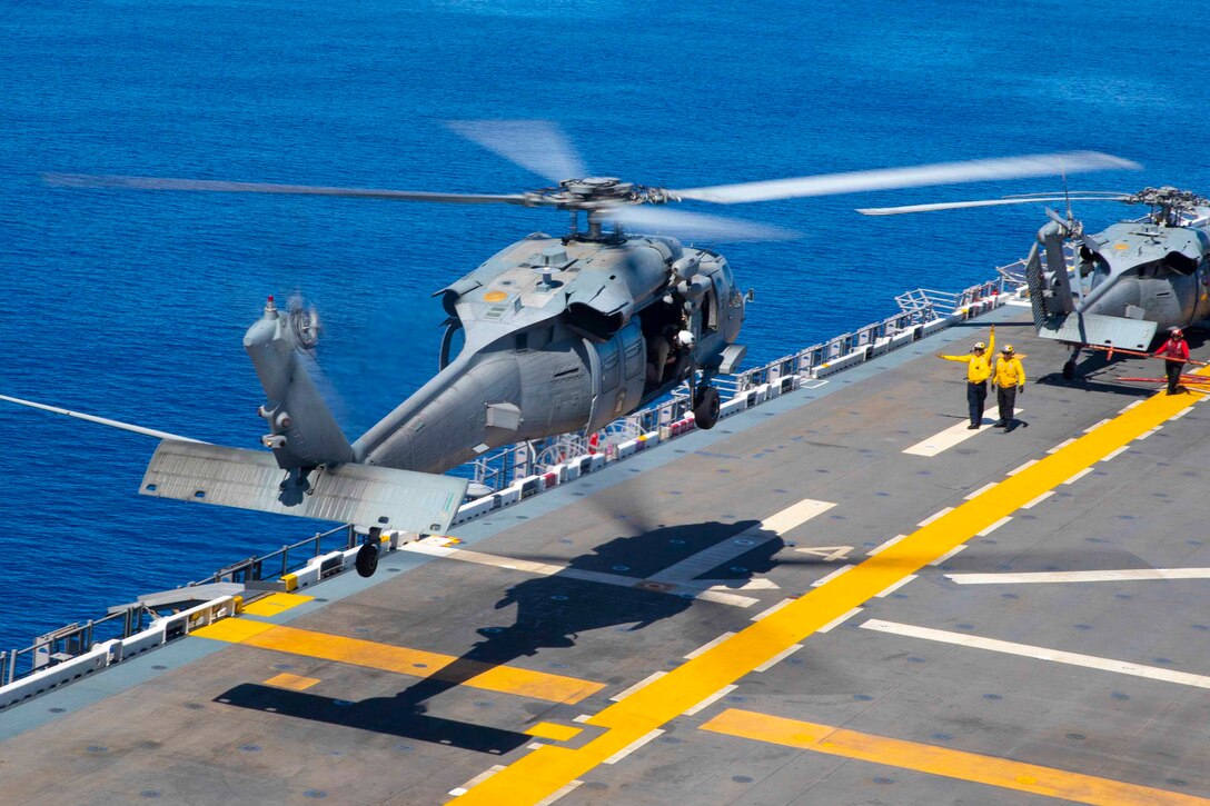 A helicopter hovers over the deck of a ship.