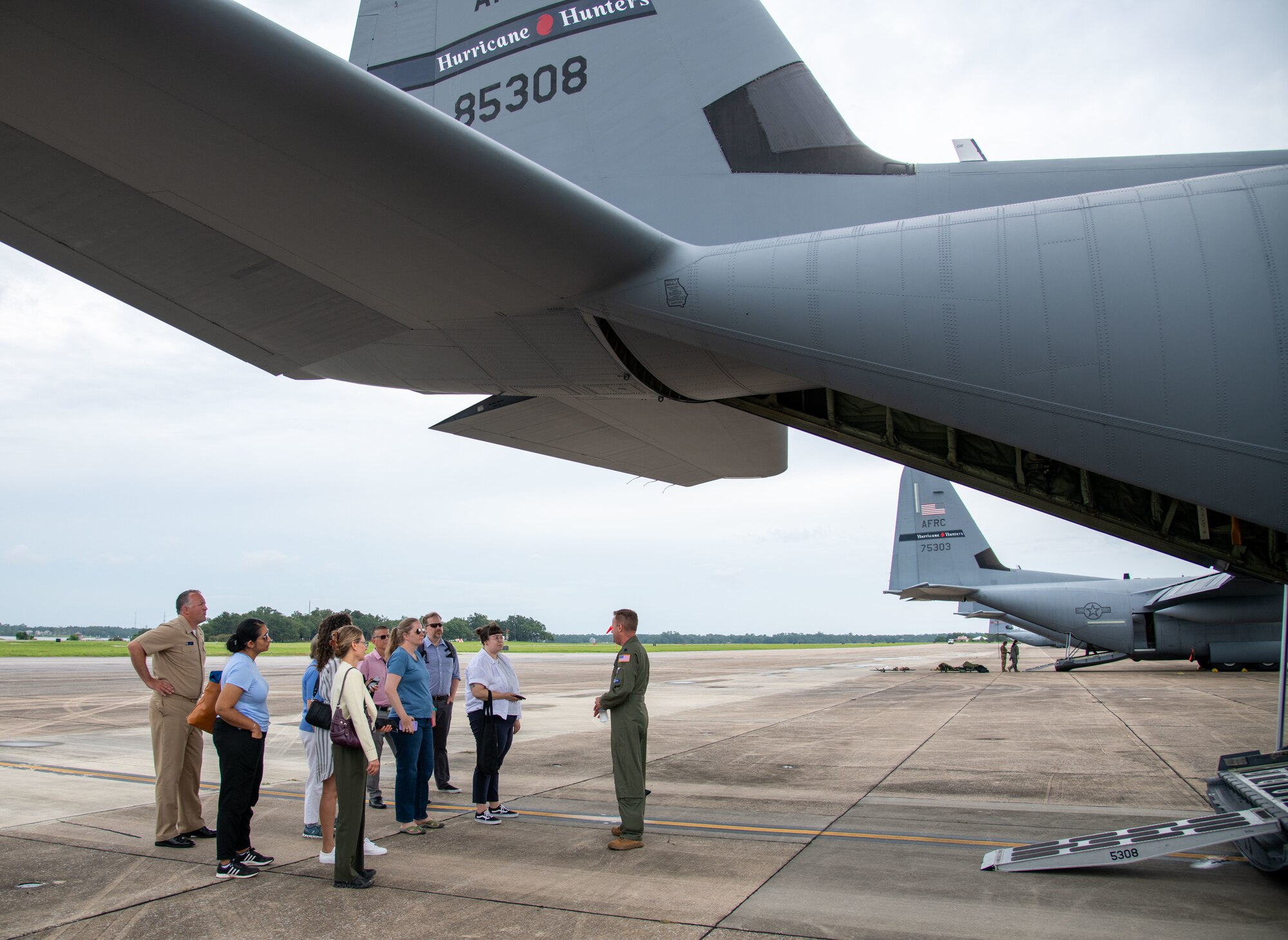 A group stands under the tail of a WC-130J aircraft