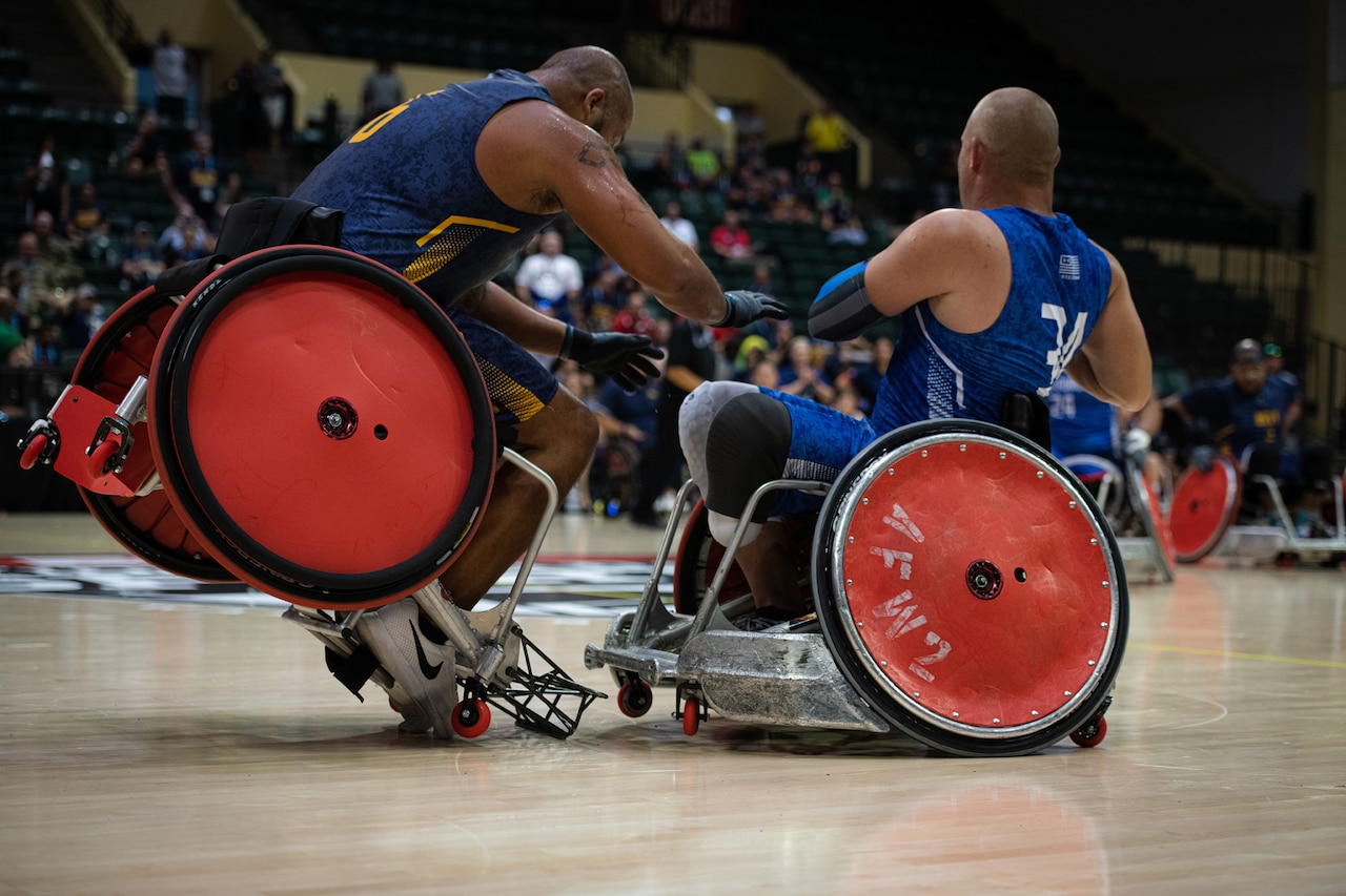 Two athletes crash their wheelchairs on an indoor court.