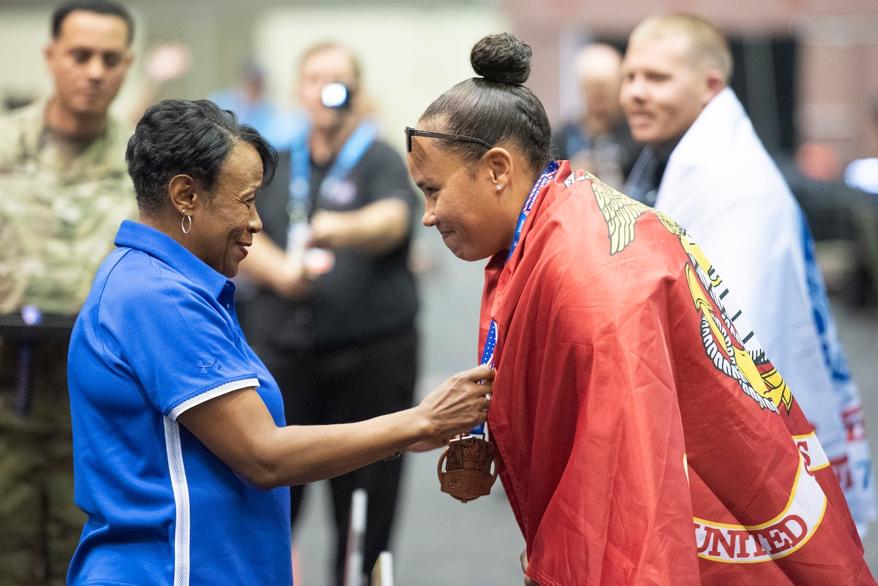 A person puts a medal around the neck of a Marine with a Corps flag draped around her.