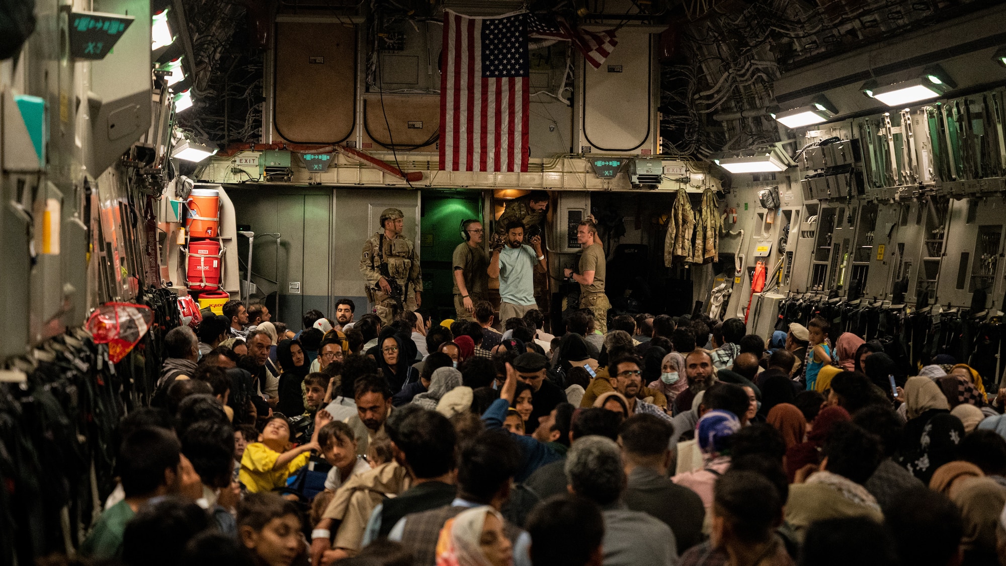 U.S. Air Force Airman discuss the situation as Afghan citizens rest after being evacuated from Hamid Karzai International Airport in Kabul, Afghanistan, Aug. 19, 2021. The U.S. Air Force conducted airlift operations to transport approximately 124,000 people from Kabul as part Operation Allies Refuge. The operation was one of the largest air evacuations of civilians in American history. (U.S. Air Force photo by Staff Sgt. Brandon Cribelar)