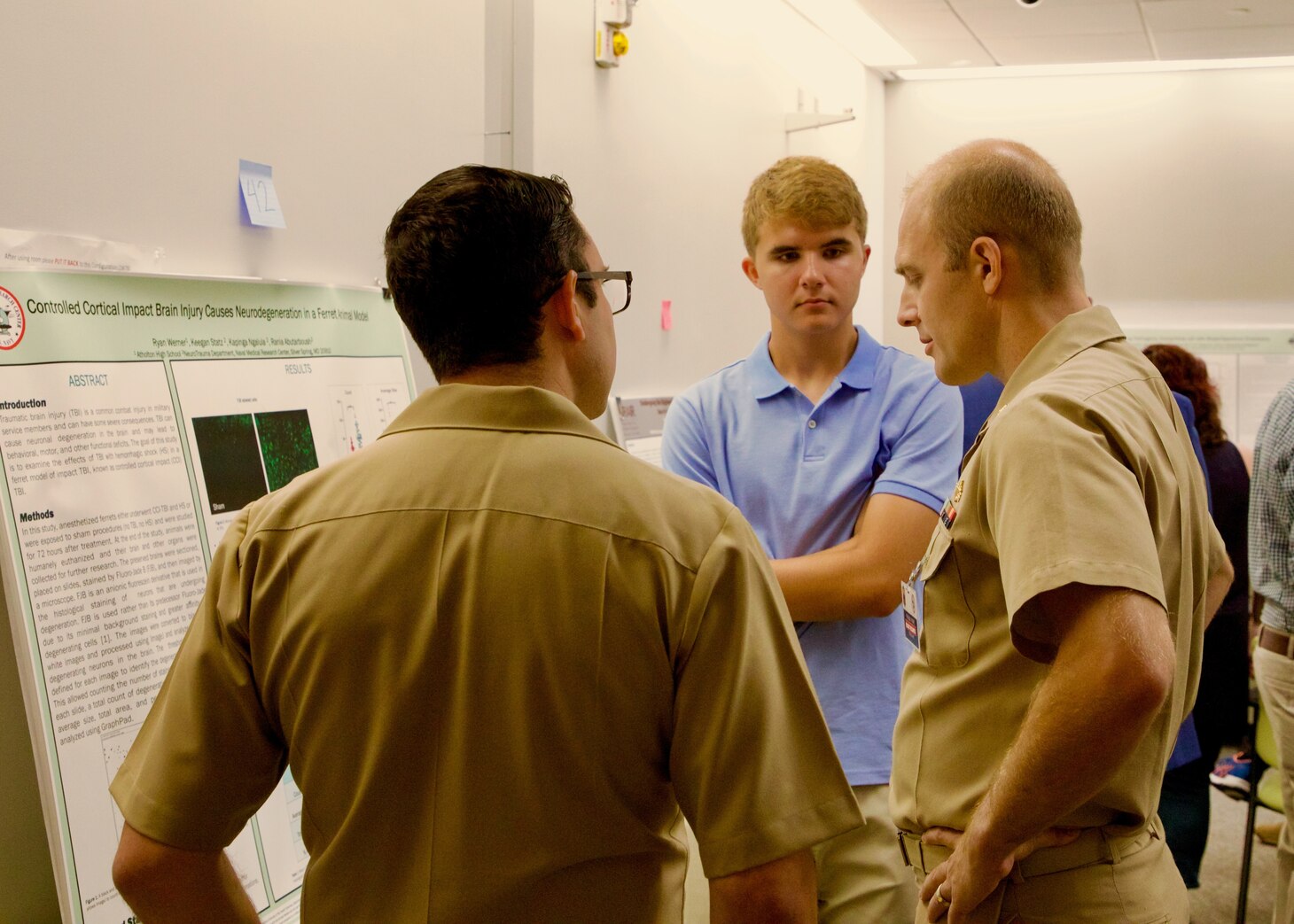 Ryan Werner (center), an intern with the Naval Research Enterprise Internship Program (NREIP) explains findings from a research poster to Naval Medical Research Center (NMRC) staff. Interns from NMRC and Walter Reed Army Institute of Research presented on research they participated in at an annual joint STEM Expo Poster Session, which marked the final day of the summer program. (U.S. Navy photo by Sidney Hinds/Released)