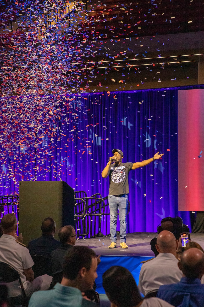 A person speaks on stage as confetti pours down.