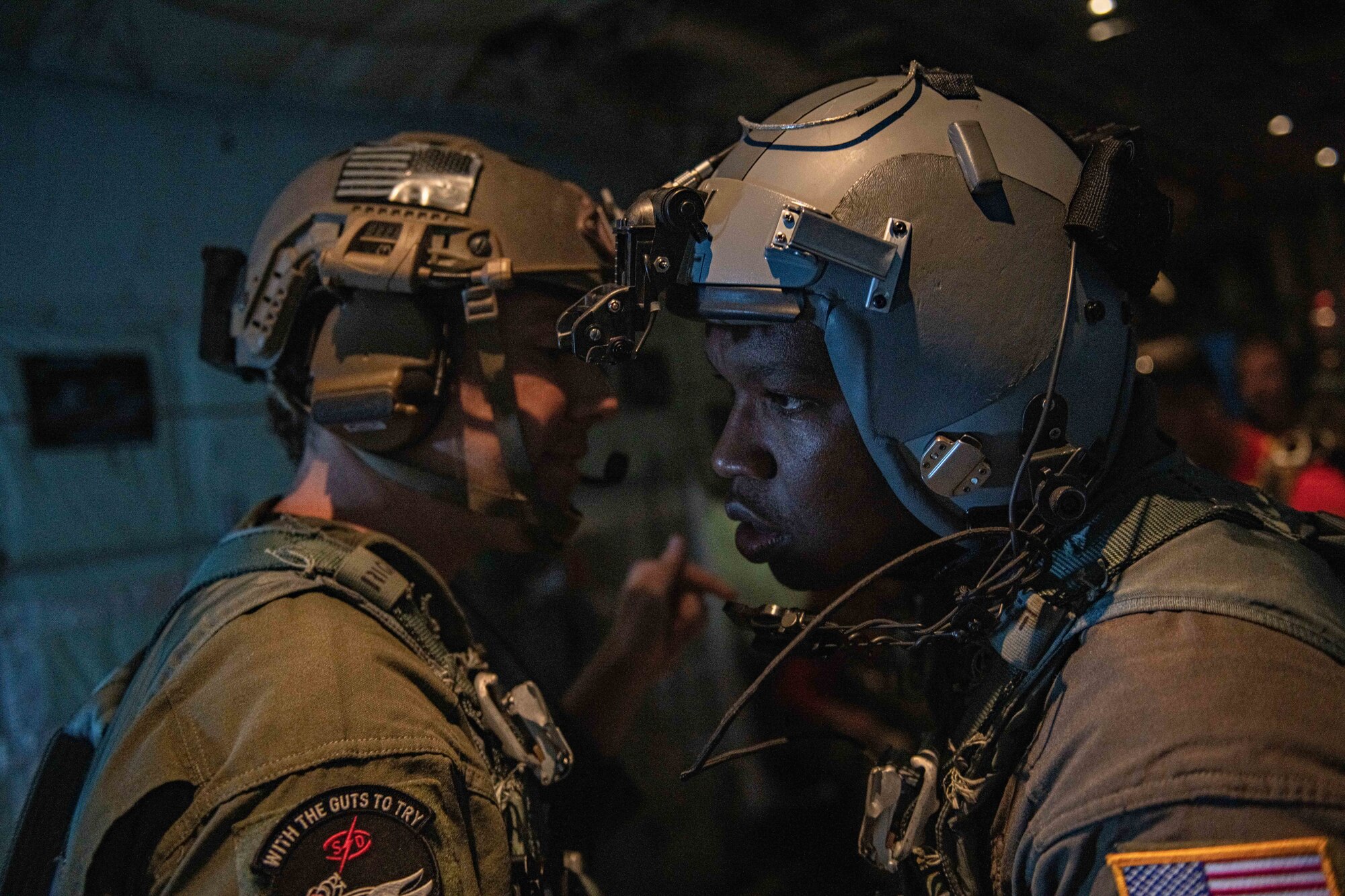 Two airmen discuss in the dark of the belly of the plane, the drop zone and plans to unload Airmen and gear safely.