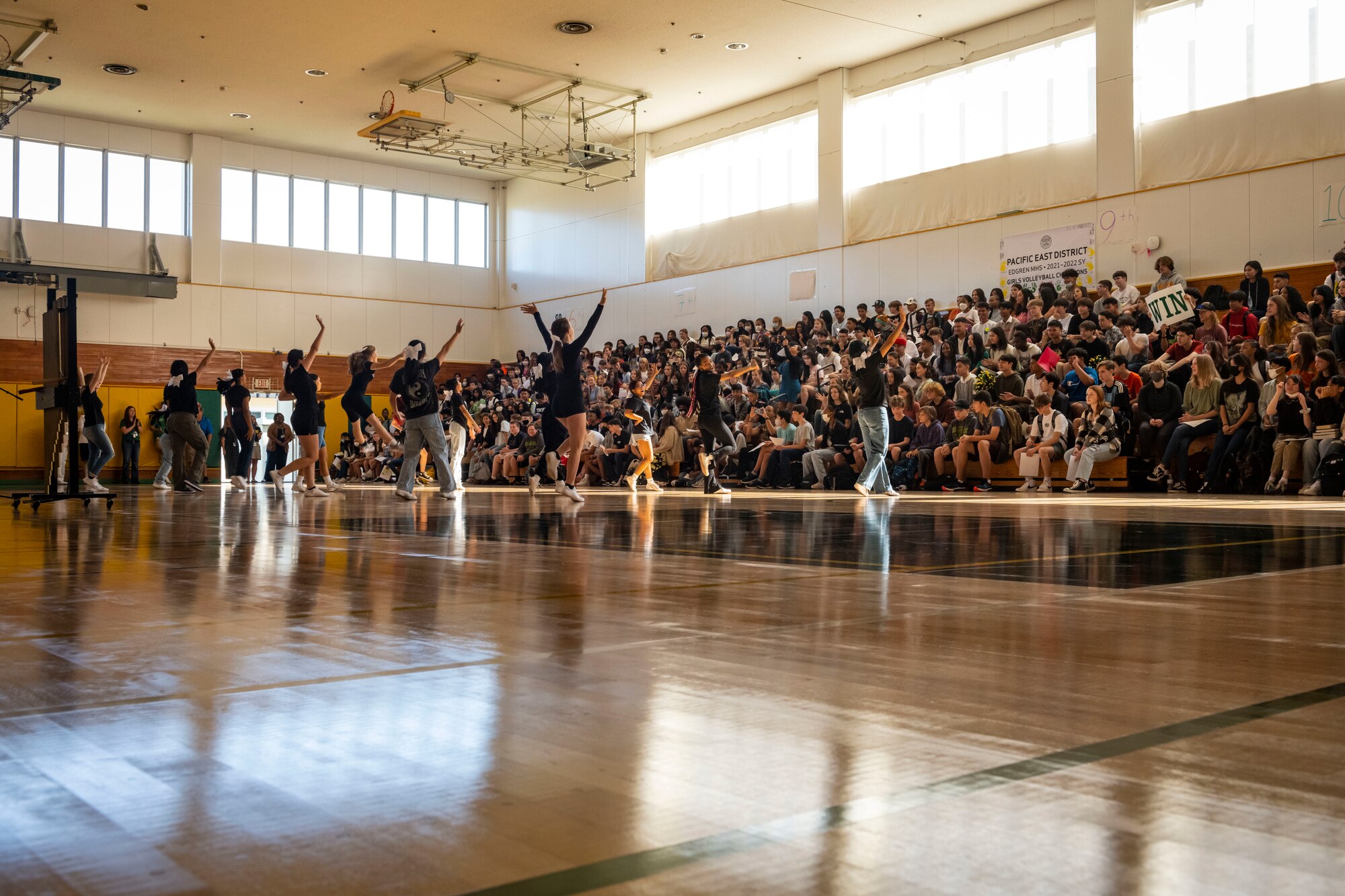 Students dance in a gym with people watching from bleachers