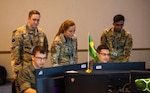 Air Force Capt. Leah Elsbeck, center, and Senior Airman Dhruva Poluru, members of the New York Air National Guard’s 222nd Command and Control Squadron, watch as members of the Brazilian military’s space control team solve a problem during the U.S. Space Command’s Global Sentinel exercise at Vandenberg Space Force Base in July 2022. Elsbeck and Poluru, along with Capt. Victoria Whelan, served as mentors during the exercise.