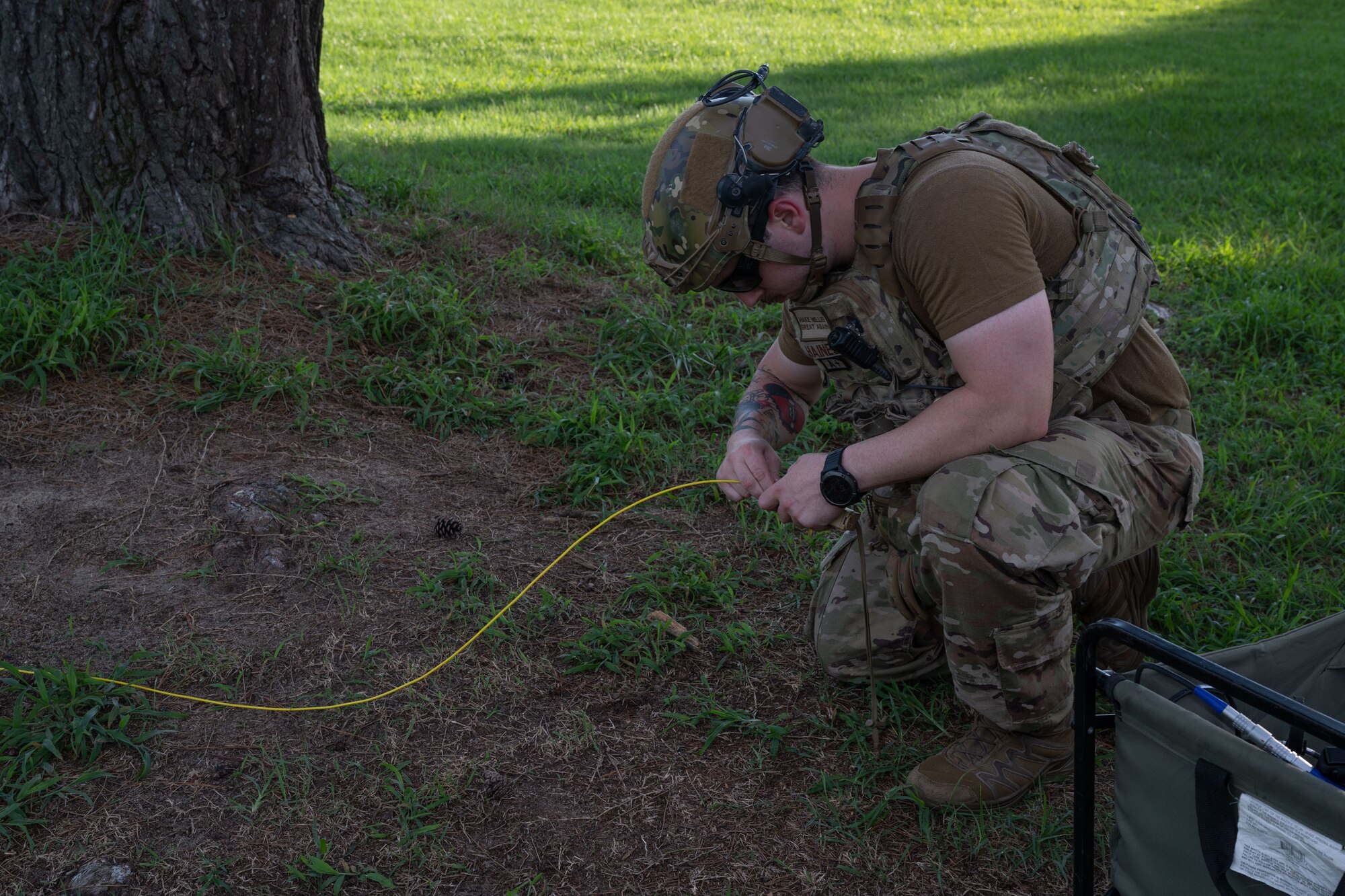 An Airman connects a yellow cord to an explosive tool, preparing to ignite the simulated explosive package.