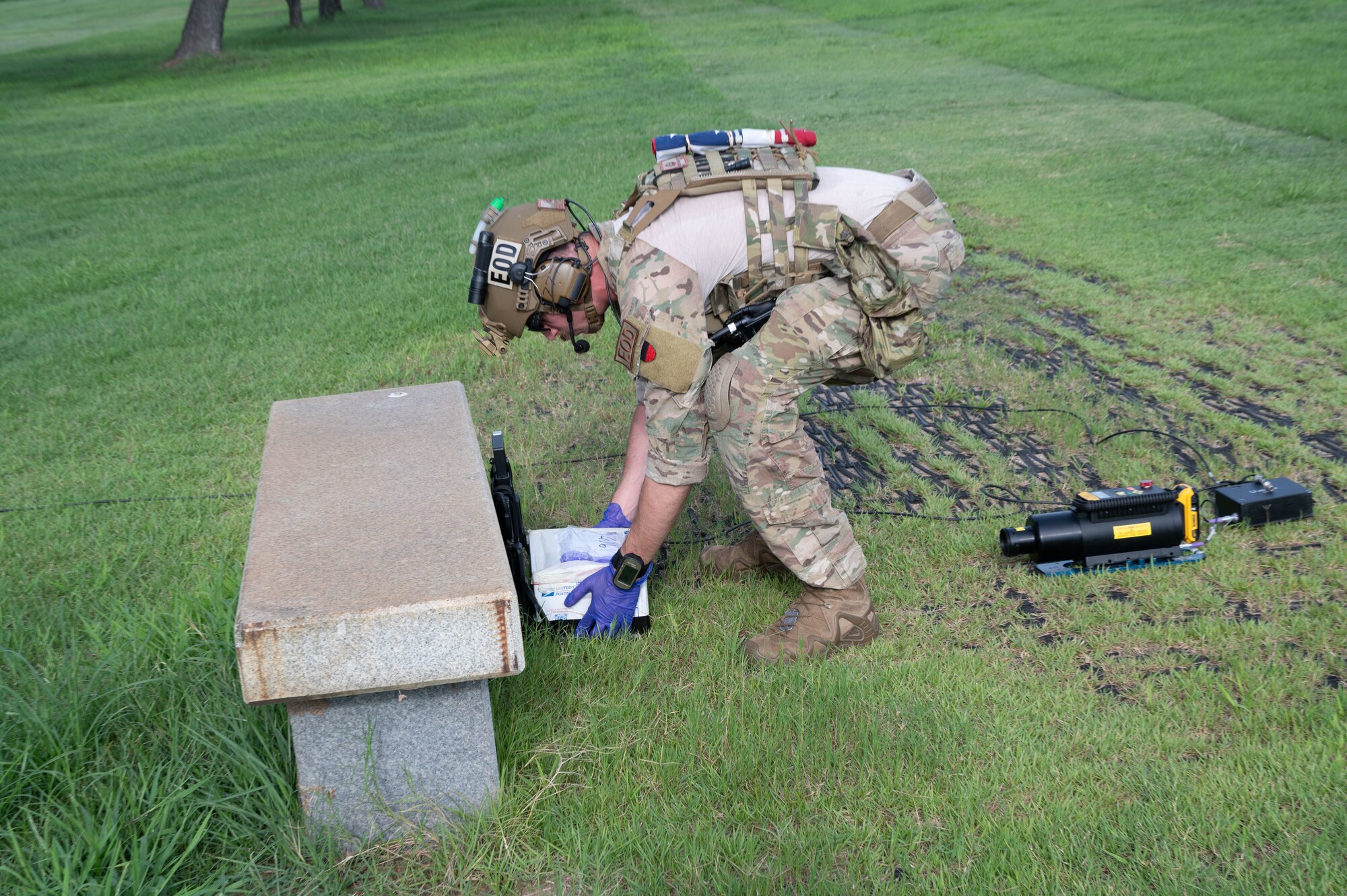 An Airman places a simulated explosive package on the ground in front of a x-ray generator.