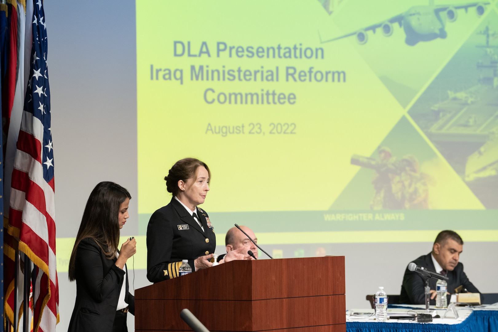 Woman speaks from a podium with a slideshow in her background.