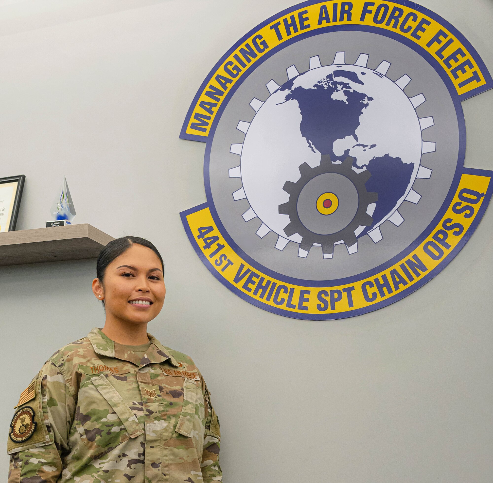 U.S. Air Force Tech. Sgt. Jennifer Gloria “JT” Thomas, 441st Vehicle Support Chain Operations Squadron, noncommissioned officer in charge of vehicle disposition and lease management, stands under the 441st VSCOS seal at Joint Base Langley-Eustis, Virginia.