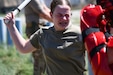 A female soldier with her eyes nearly closed due to being sprayed with OC spray, uses a baton to engage a simulated adversary .