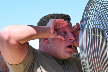 A soldier holds his eyes open with his fingers in front of a fan to air his eyes off after being sprayed with OC.