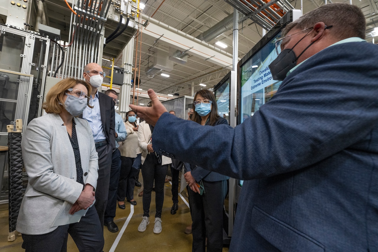Multiple people stand near each other for a discussion in an industrial area.