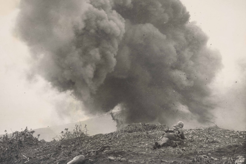 A man lies prone as smoke billows from a nearby explosion.