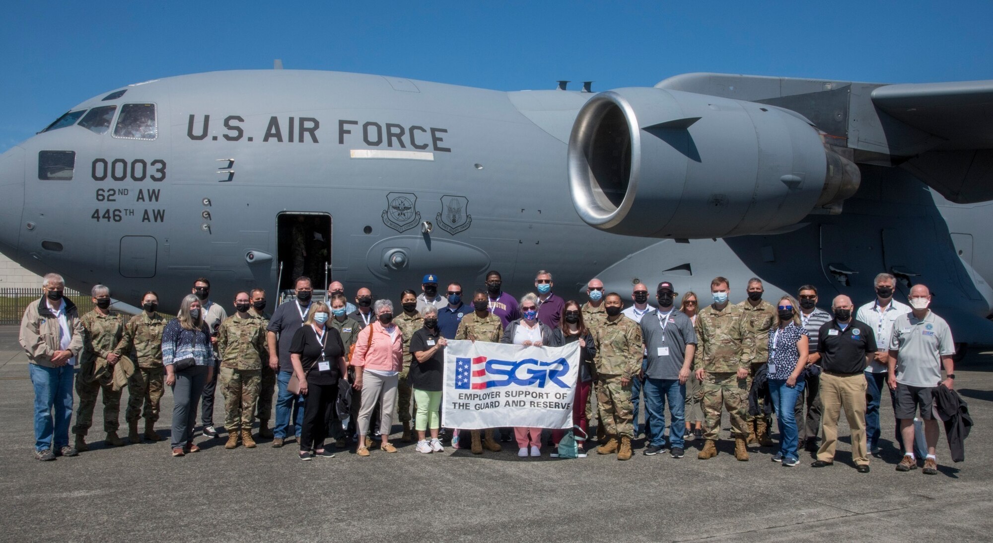 Group photo of civilians and service members holding a banner with the letters 'ESGR' in front of an aircraft.