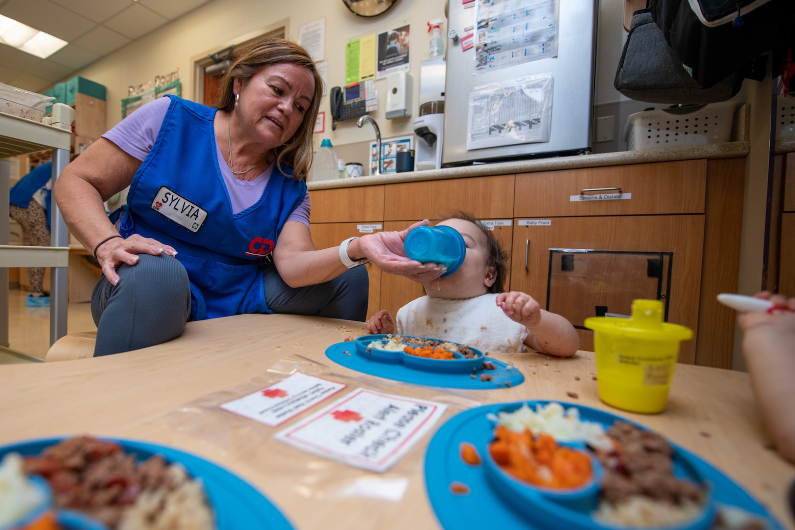 female teacher feeds a toddler a bottle of milk