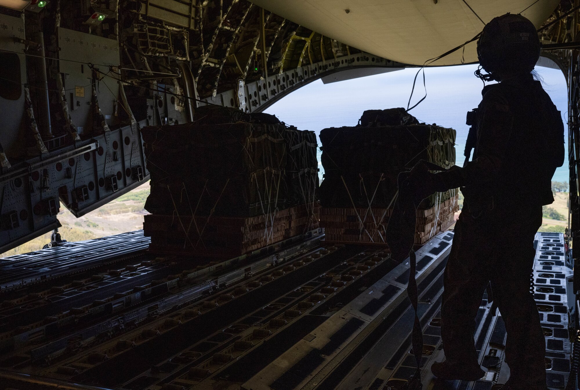 Senior Airman Jolan Besse, 535th Airlift Squadron loadmaster, observes container delivery system bundles exiting a C-17 Globemaster III during an airdrop training exercise at Kane’s Drop Zone, Kahuku, Hawaii, Aug. 24, 2022. Aircrew from the 535th Airlift squadron conducted training by performing an airdrop of container delivery system bundles of supplies. (U.S. Air Force photo by Senior Airman Makensie Cooper)