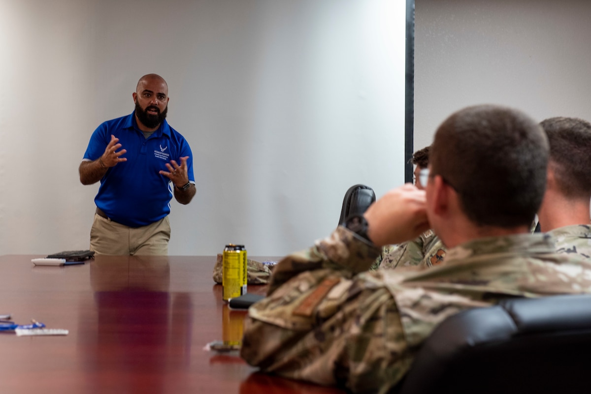 A man in a blue shirt expresses himself to a group of airman wearing ocps.