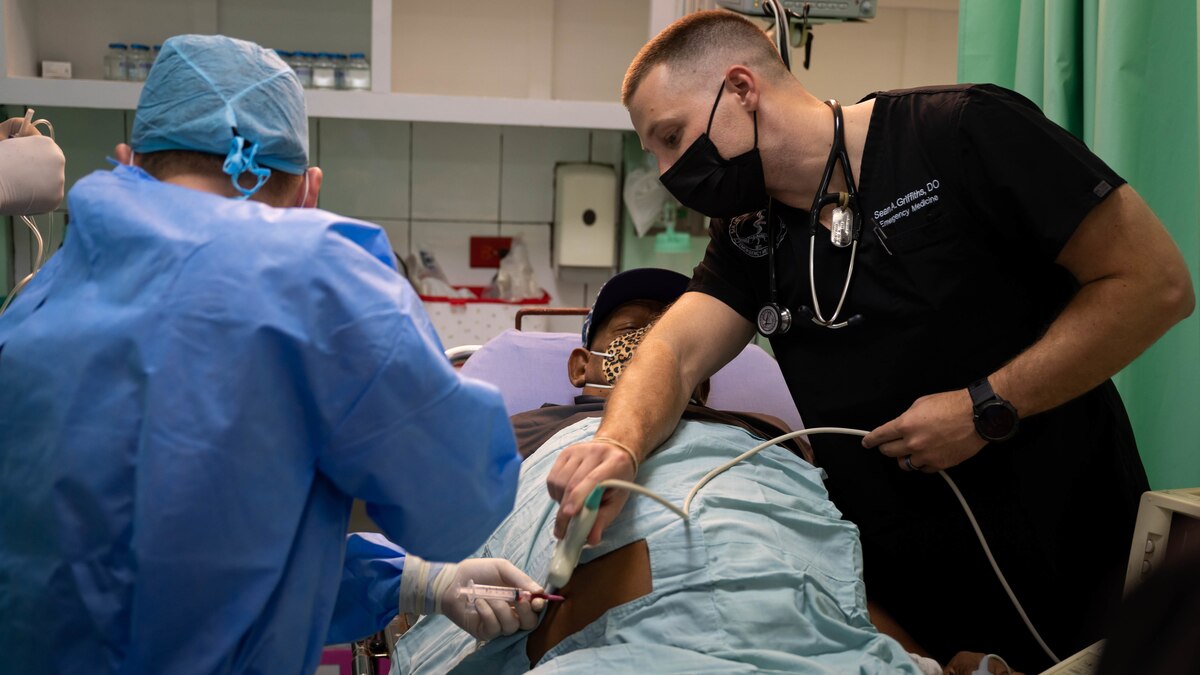 Photo of U.S. Air Force Capt. Sean Griffiths (right), 959th Emergency Medicine Squadron emergency medicine physician, helps a patient alongside El Salvadorian medics at the Hospital Militar Central in San Salvador, El Salvador, June 7, 2022.