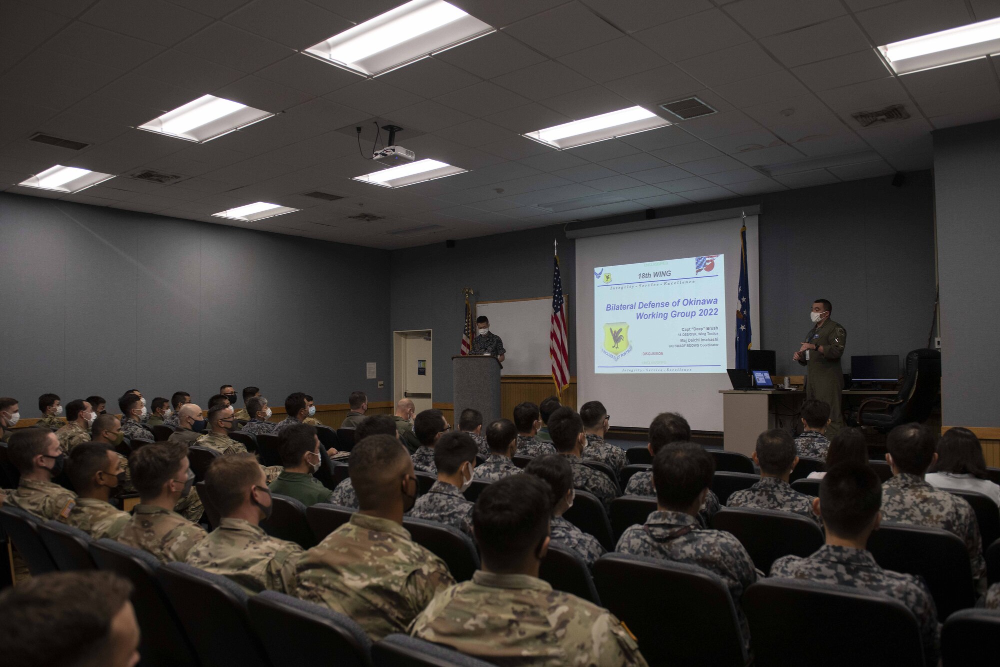 A group of Japanese and American military members sit through a brief