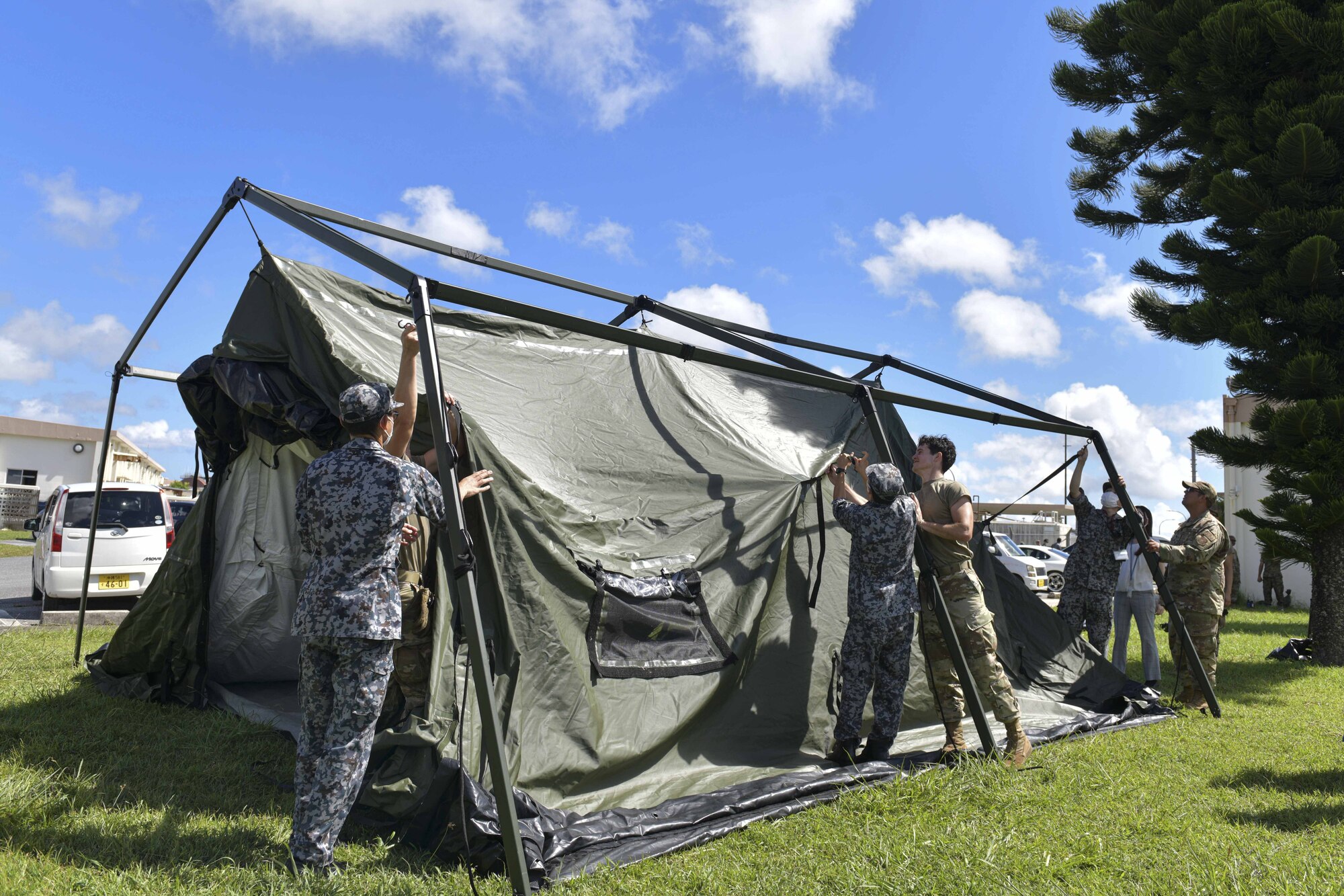 A group of Japanese and American military personnel work together to setup a tent