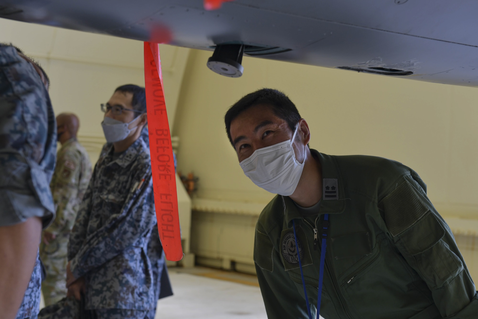 A Japanese military member smiles as he inspects the bottom of an F-15