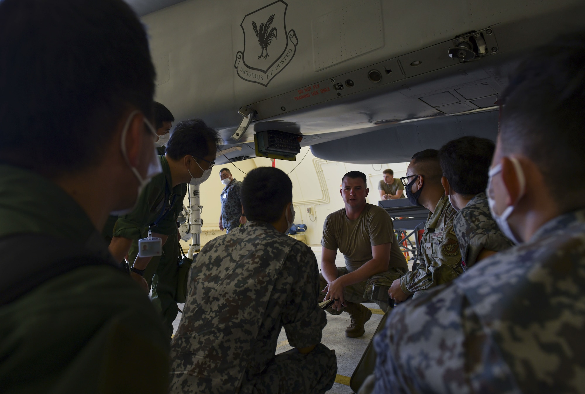 A U.S. Air Force member stoops under an F-15 to explain how refueling on the ground works to Japanese military personnel