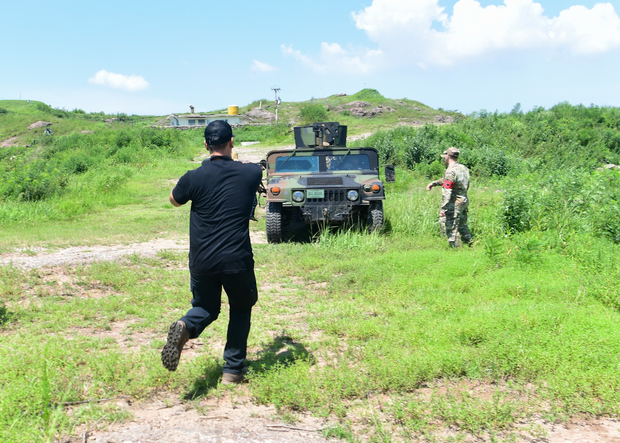 A individual in civilian attire portraying an adversary approaches an armored military vehicle during a training event.