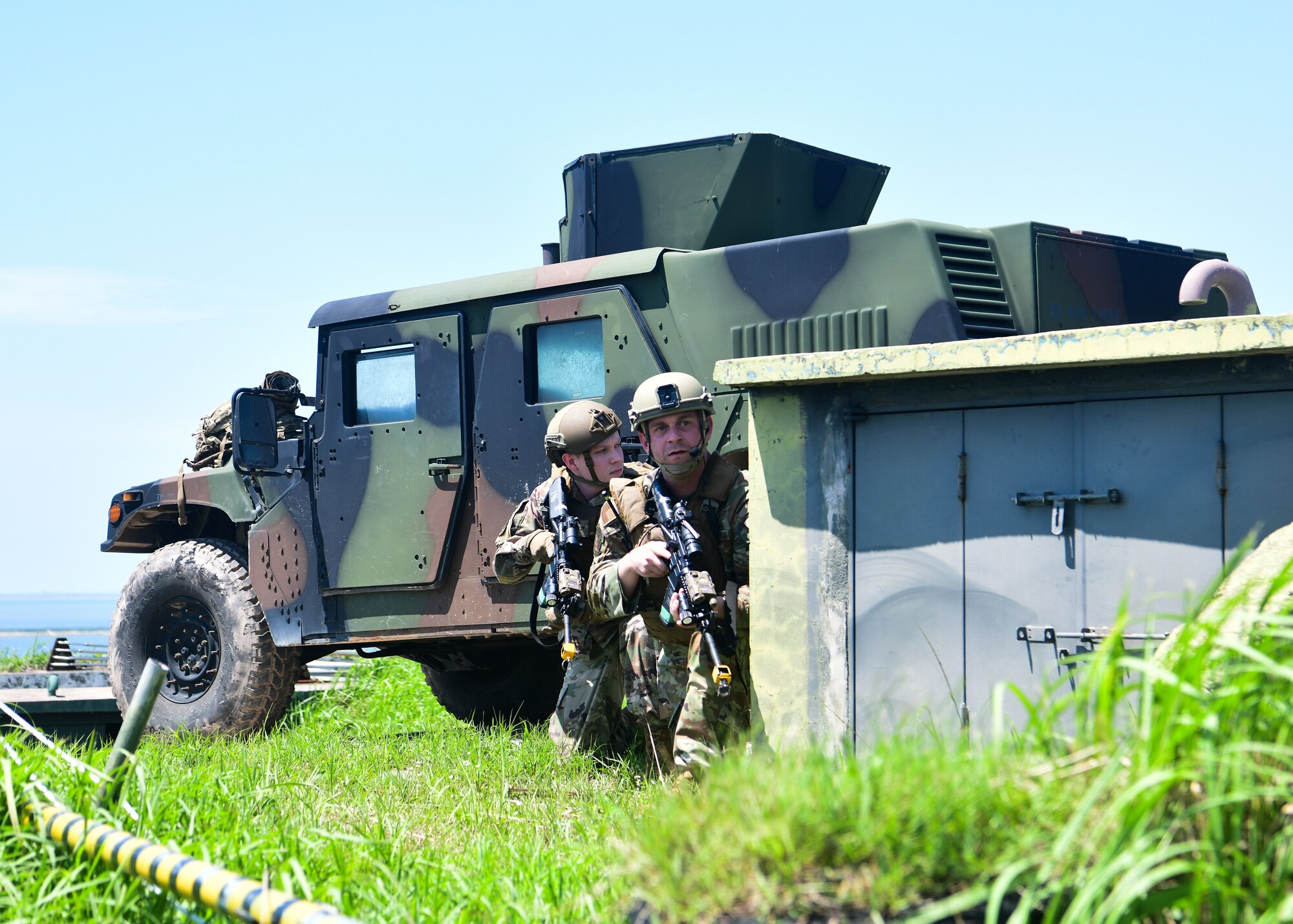 Military police officers hide behind cover with weapons drawn during a training event.