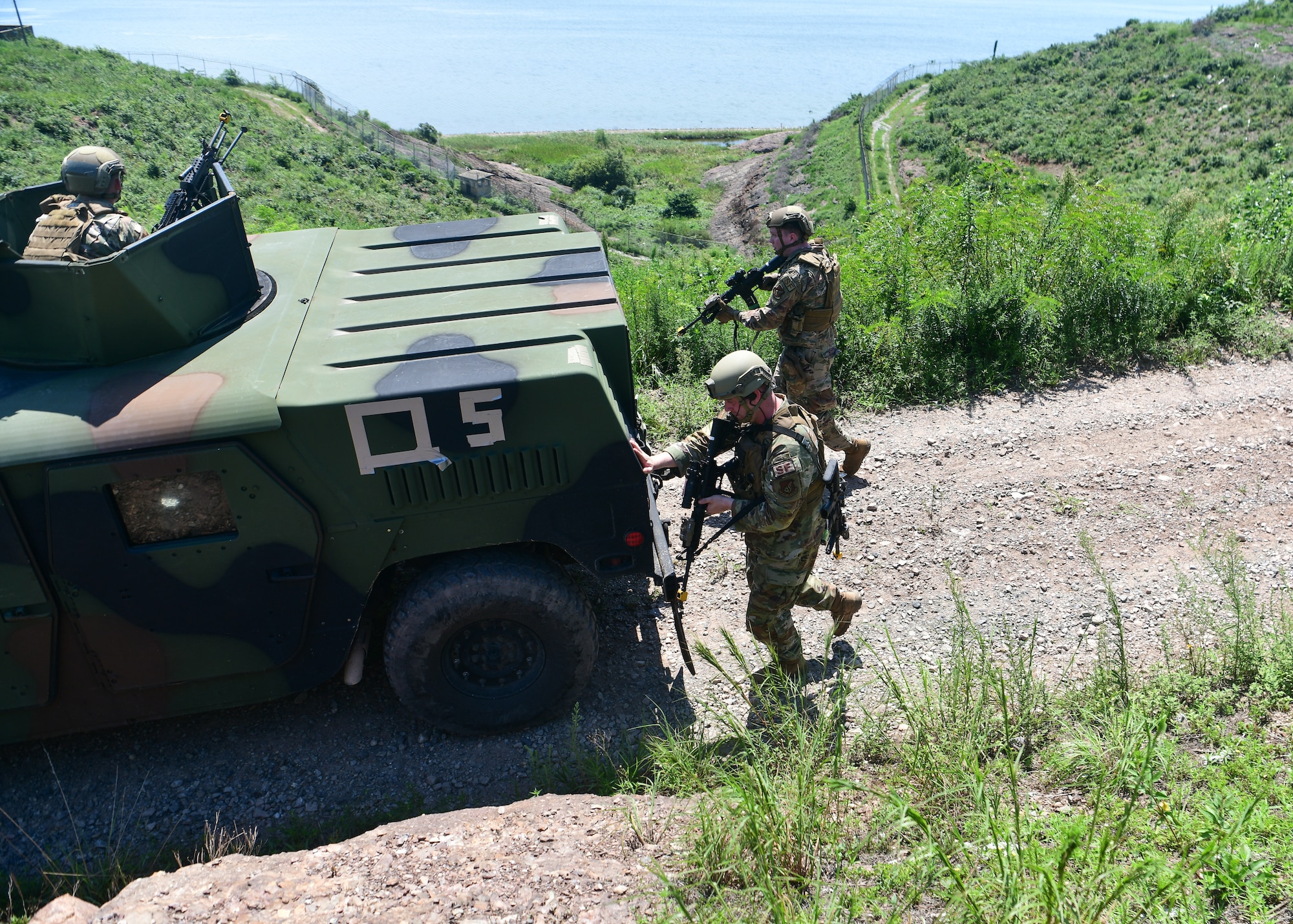 Military police officers walk behind an armored military vehicle during a training event with weapons drawn.