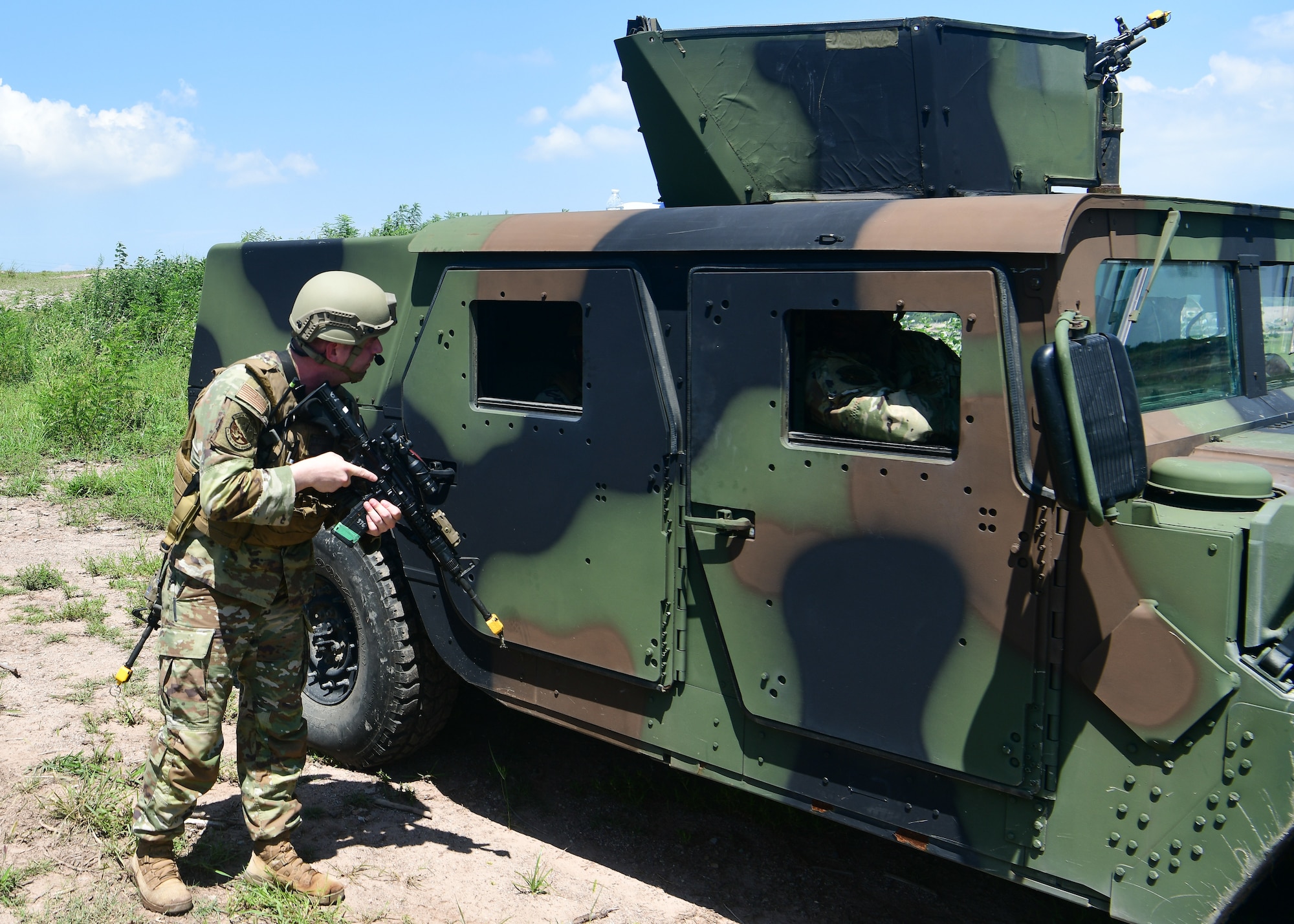 A military police officer approaches an armored military vehicle with a weapon drawn.