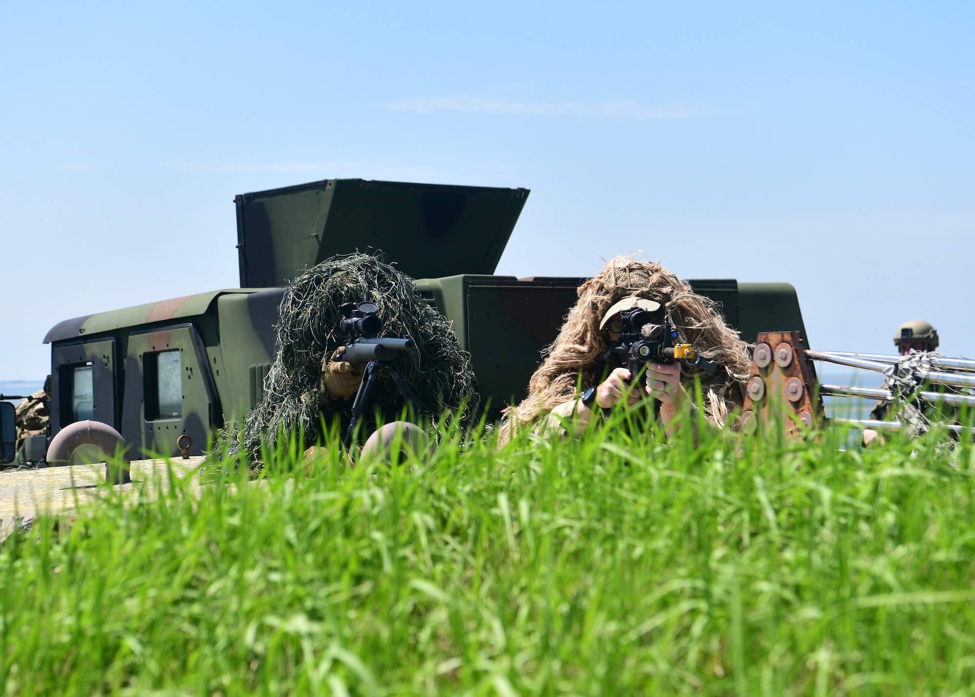 Military members with camouflage look through lenses past the camera.